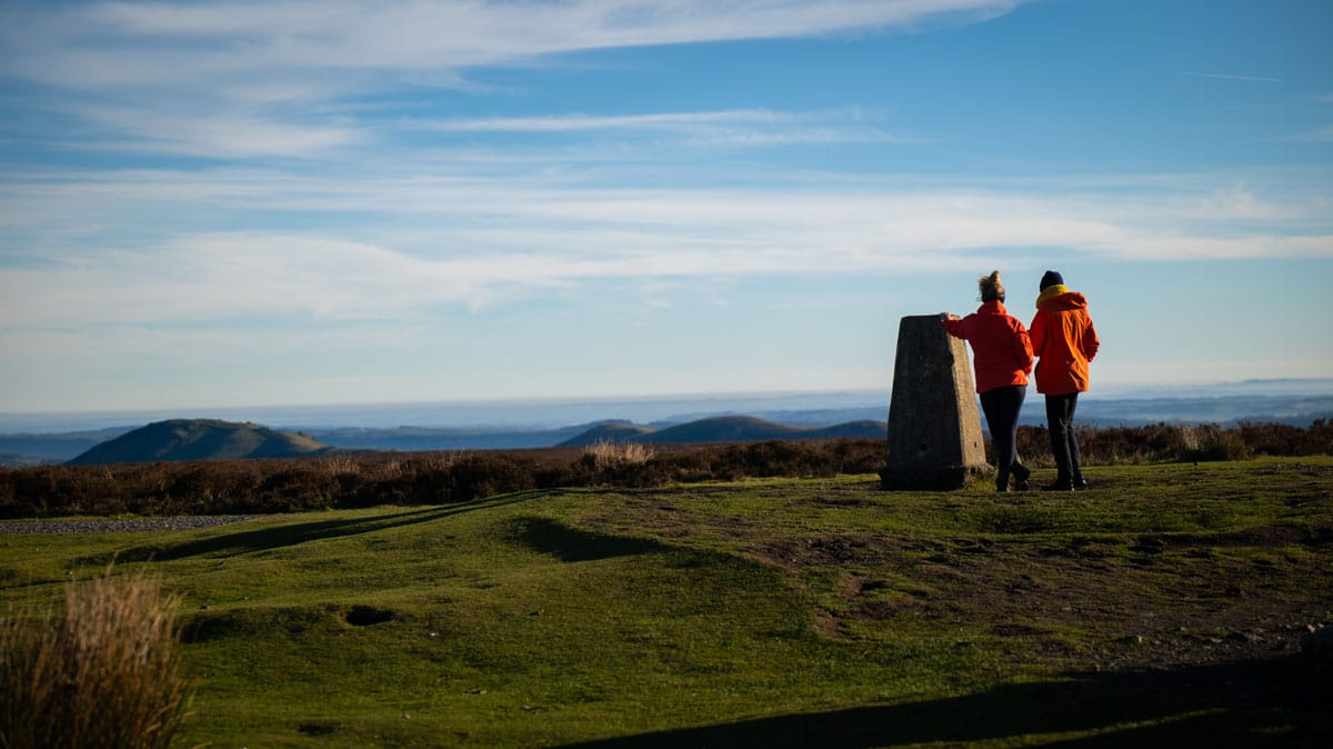 2 people standing at Trigpoint on long mynd<br />
