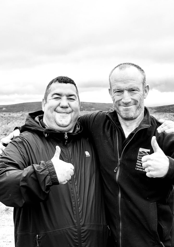 Two men smile at the camera with their thumbs up