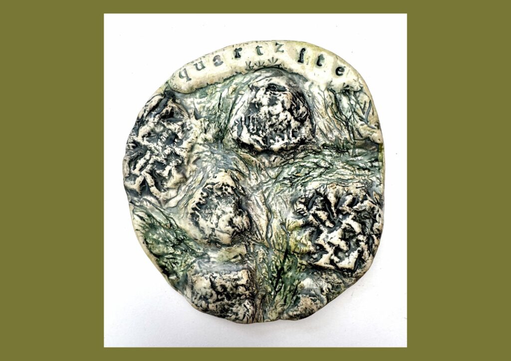 A circular organic shaped ceramic plaque is decorated with green and brown glazes and raised textured elements that depict the sharp rocks in the landscape.