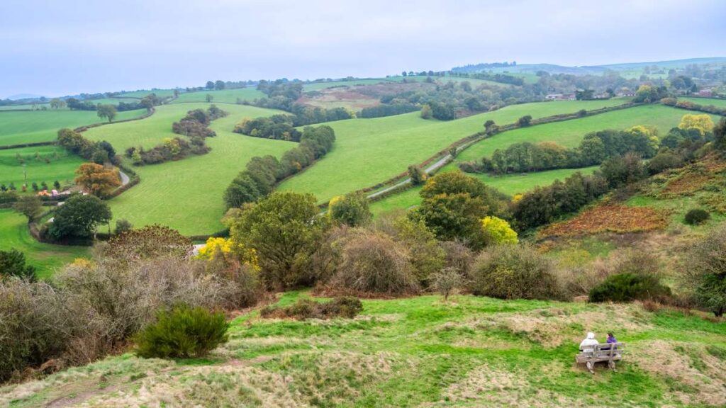 Photo of a view from the top of the motte-and-bailey mound at Castle Pulverbatch. A bench with two people sat on is also visible in the picture.