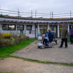 3 people outside the Discovery centre by the picnic benches- one on a mobility scooter