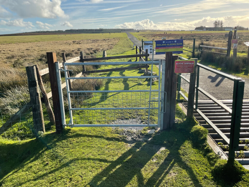 Photo showing a gate that serves as an entrance to the gliding club with the airfield behind.